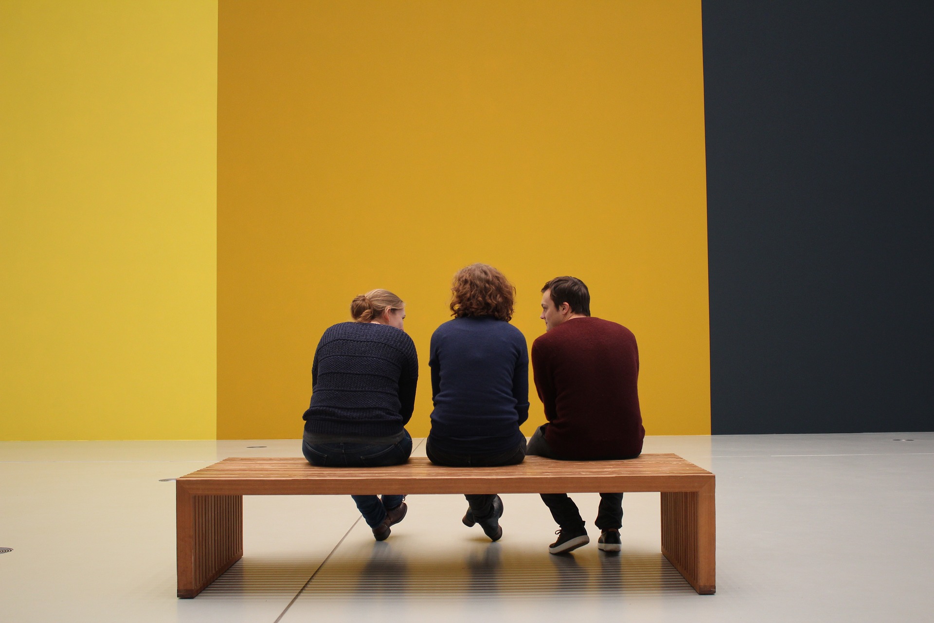 Tre personer på en bänk framför en gul vägg 