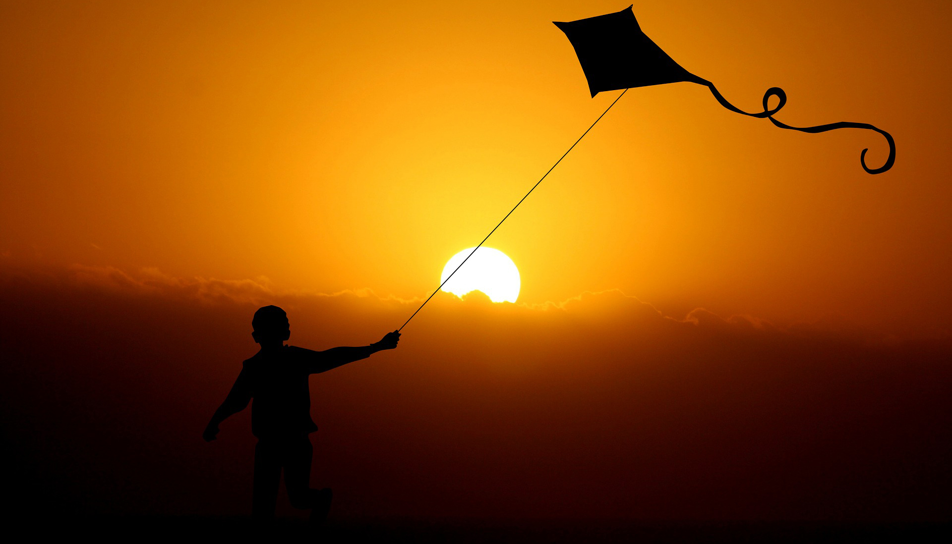 Ett barn håller i en drake, en solnedgång i bakgrunden
