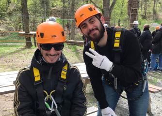 Två leende unga män med orange hjälmar och säkerhetsutrustning
