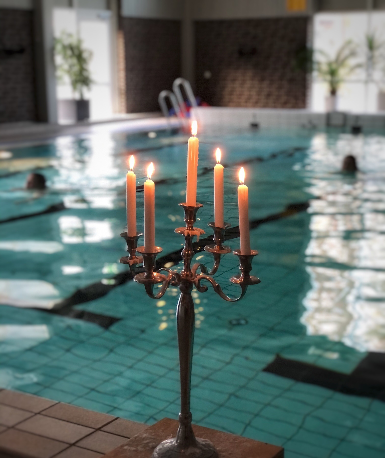En kandelaber med tända ljus med en simbassäng i bakgrunden