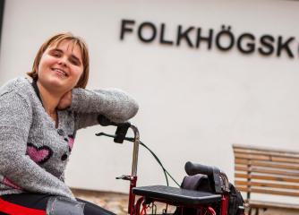 Tjej sitter på en permobil och ler in i kameran
