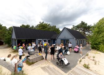 Personer uppehåller sig runt Strandstugan i väntan på att surfen ska starta.